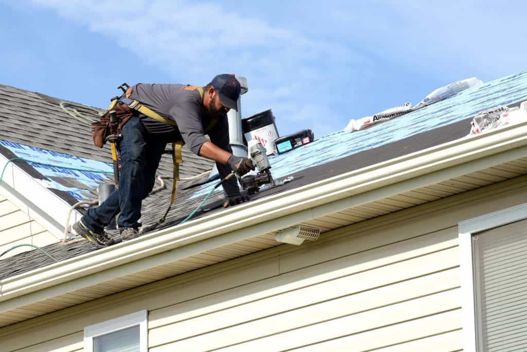 Are roof ridge vents necessary? - a man working on a roof installation with tools sitting on the roof