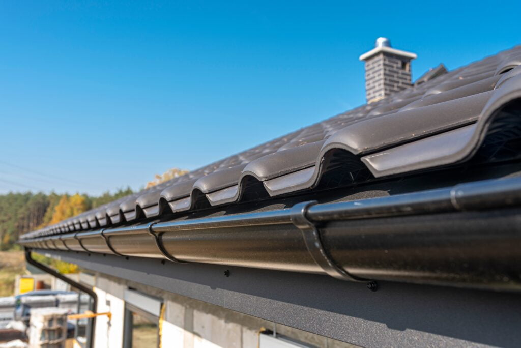 What is the Lifespan of a Commercial Roof? - The edge of a dark charcoal metal roofing system with a matching dark charcoal metal gutter system.