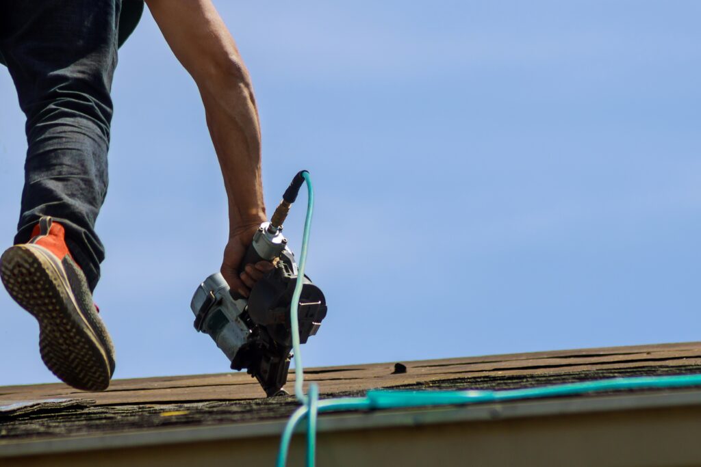 Hail damage roofing contractors near roseville, mn - a man walking up a roof with a nail gun in hand